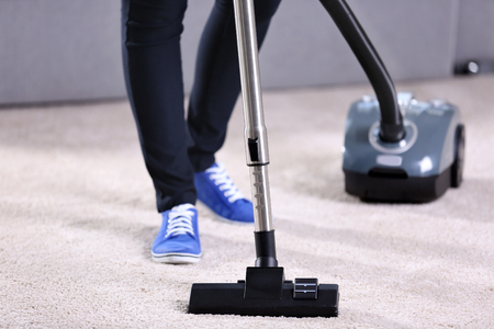 Woman using vacuum cleaner on carpet at home in the living room, close upの写真素材