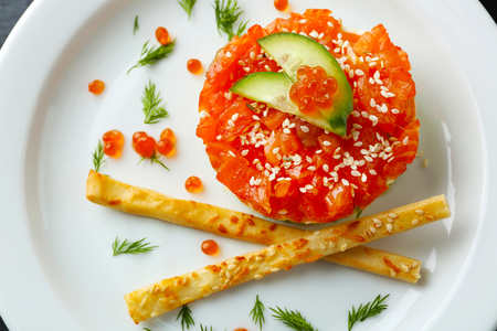 Fresh tartar with salmon, avocado, cucumber and red caviar on white plate, close upの写真素材