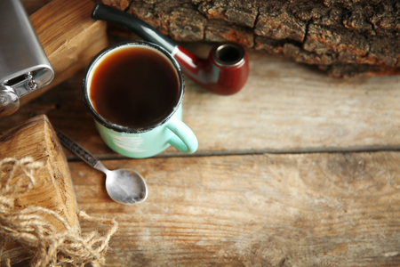 Metal mug of coffee with flask and tobacco pipe on wooden backgroundの写真素材