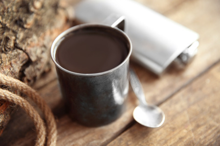 Metal mug of coffee with flask, spoon and rope on wooden backgroundの写真素材