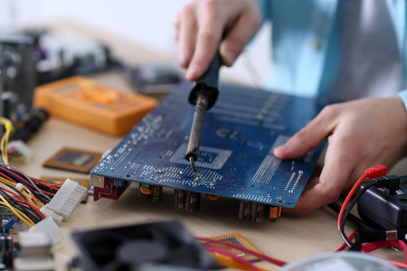 Young man working with soldering iron in service center