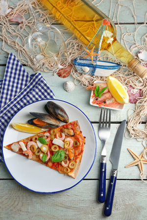 Pizza slice with seafood, red pepper, green olives and bottle of wine on wooden tableの写真素材