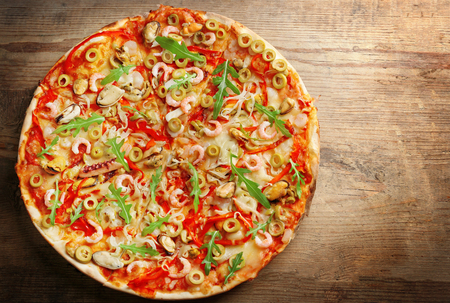 Pizza with seafood, red pepper and green olives on wooden tableの写真素材