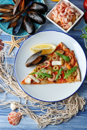 Pizza slice with seafood, red pepper and green olives on blue wooden tableの写真素材