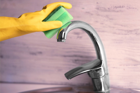 Female hand with sponge cleaning a tap in the kitchenの写真素材