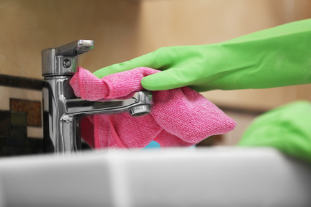 Female hands with rag cleaning a tap in the bathroomの写真素材