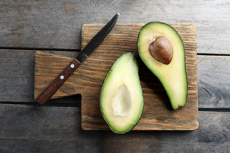 Sliced avocado with knife on wooden cutting board