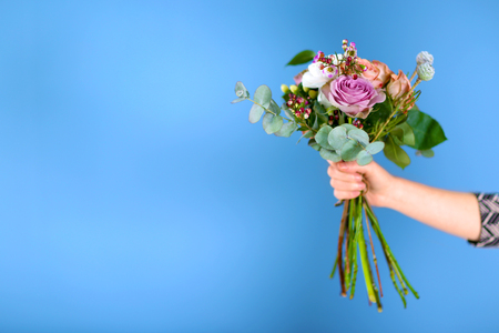 Female hand holding a bouquet of roses on blue backgroundの写真素材