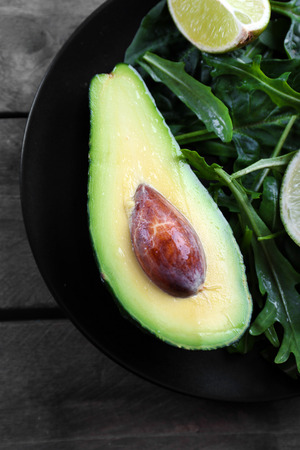 Sliced avocado with lime, spinach and arugula on black plateの写真素材