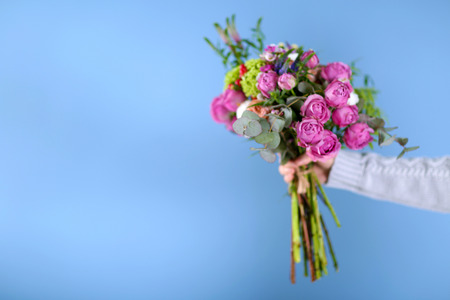 Female hand holding a bouquet of roses on blue backgroundの写真素材