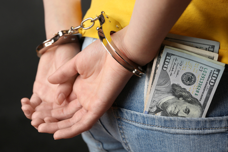 Hands in handcuffs behind back and dollar banknotes on the pocket, close up. Corruption conceptの写真素材