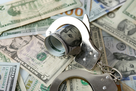 Handcuffs with rolled dollar banknote on paper background. Corruption concept