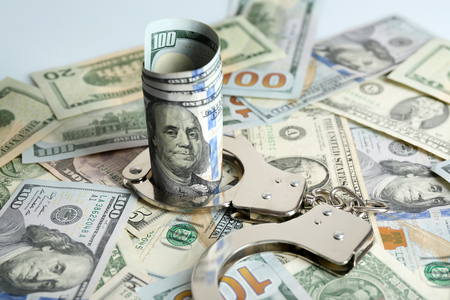 Handcuffs with rolled dollar banknote on paper background. Corruption conceptの写真素材