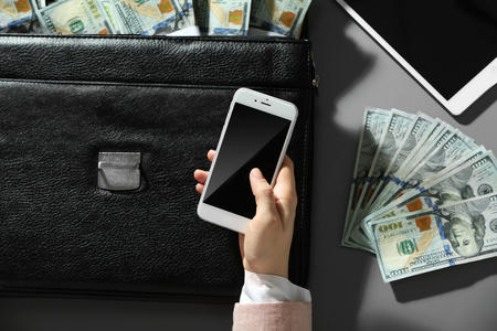 Businesswoman holding cellphone and brief case with moneyの写真素材