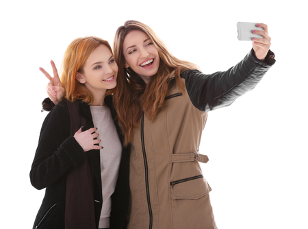Two young women taking selfie in their winter clothes isolated on whiteの写真素材