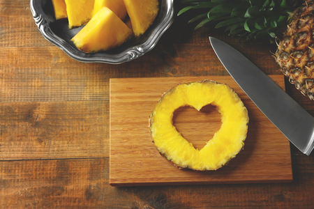 Juicy pineapple slice with cut out heart shape on wooden cutting boardの写真素材