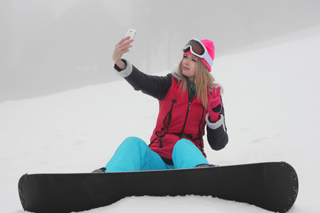 Young girl snowboarder making selfie over white snow backgroundの写真素材