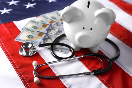 Stethoscope with dollar banknotes and piggy bank on background of USA flagの写真素材