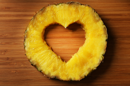 Juicy pineapple slice with cut out heart shape on wooden cutting boardの写真素材