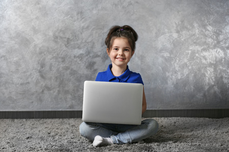 Little girl with laptop on fur carpet against grey wall backgroundの写真素材
