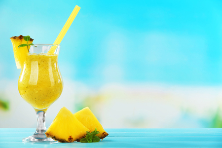 Pineapple smoothie in cocktail glass with slices on blue blurred backgroundの写真素材