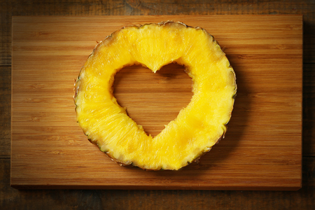 Juicy pineapple slice with cut out heart shape on wooden cutting boardの写真素材