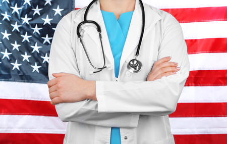 Female doctor holding in hand stethoscope with USA flag on backgroundの写真素材