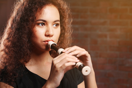 Beautiful young woman playing on recorder over brick wall backgroundの写真素材