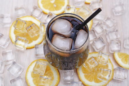 Glass of cola with ice and lemon on light wooden tableの写真素材