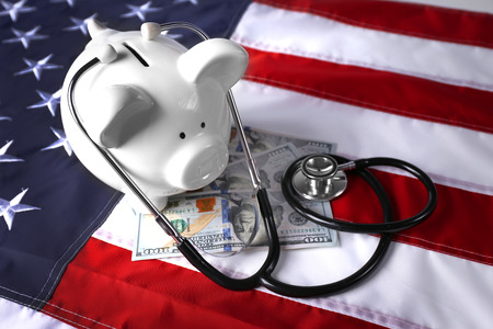 Stethoscope with dollar banknotes and piggy bank on background of USA flagの写真素材