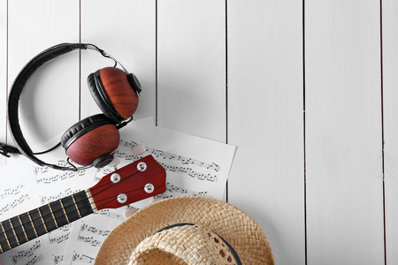 Small guitar, headphones, music sheets and straw hat on wooden surface, top viewの写真素材