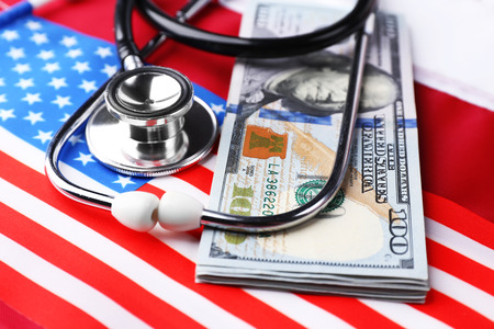 Stethoscope with dollar banknotes on background of USA flagの写真素材