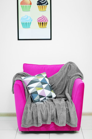 Pink armchair with blanket and pillow on light wall backgroundの写真素材