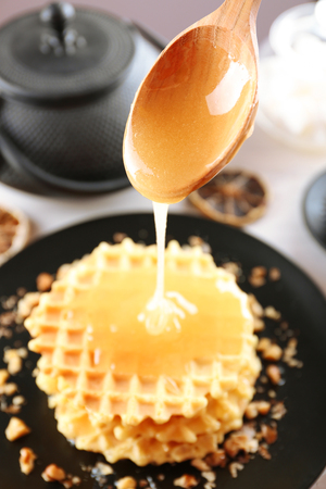 sweet honey pouring from spoon on wafflesの写真素材