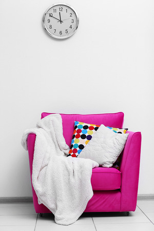 Pink armchair with blanket and pillows on light wall backgroundの写真素材