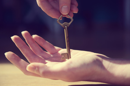 Female hand giving old key to other hand on blurred background