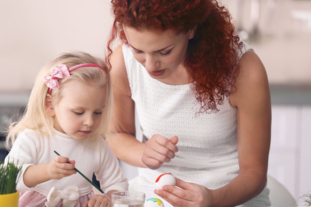 Mother and daughter decorating Easter eggs in the kitchenの写真素材