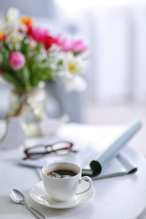 White cup of the coffee and a bouquet of flowers on wooden table  in a light room..の写真素材
