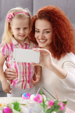 Mother and daughter making selfie while decorating Easter eggs, indoorsの写真素材