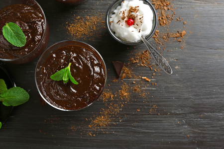 Glass cups of chocolate dessert with fresh mint and frothed milk on black wooden tableの写真素材