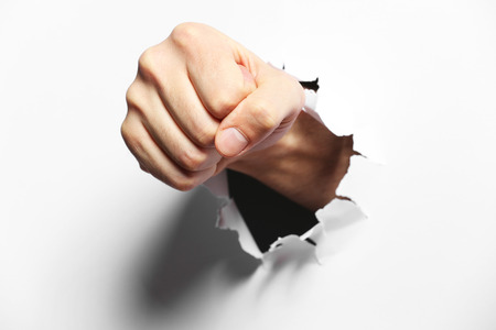 Male fist punching through paper, isolated on whiteの写真素材