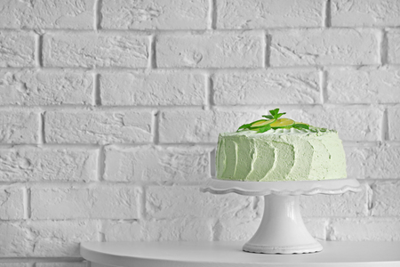 Big lime cake on a white stand beside brick wallの写真素材