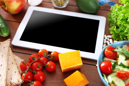 Fresh fruits and vegetables and tablet on wooden table closeupの写真素材