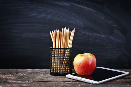 Set of pencils in metal holder, tablet and apple on blackboard backgroundの写真素材