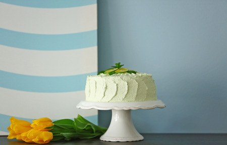Big lime cake on a white stand beside light blue wallの写真素材