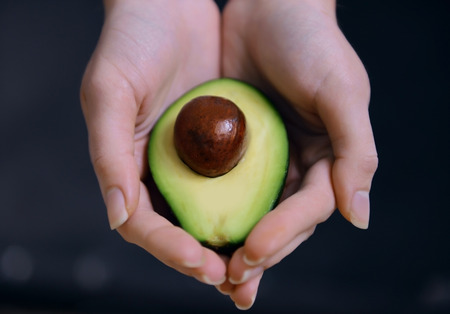 Female hands holding fresh avocado, closeup
