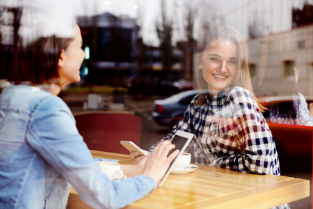 Young happy women drinking coffee and talking in cafeの写真素材