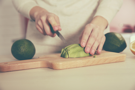 Woman slicing fresh avocado on cutting boardの写真素材