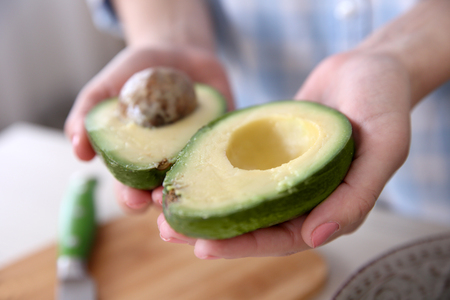 Woman holding fresh avocado in kitchenの写真素材