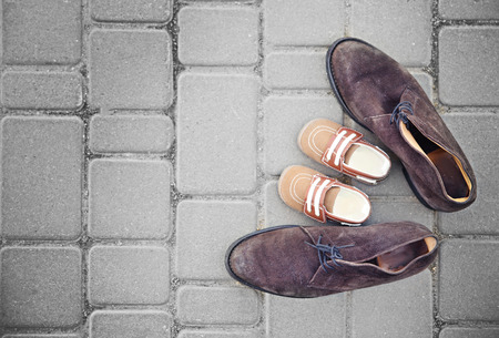 Father's shoes close to child's shoes on pavement backgroundの写真素材